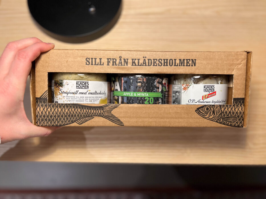 a person holding a box with three containers containing herring from klädesholmen