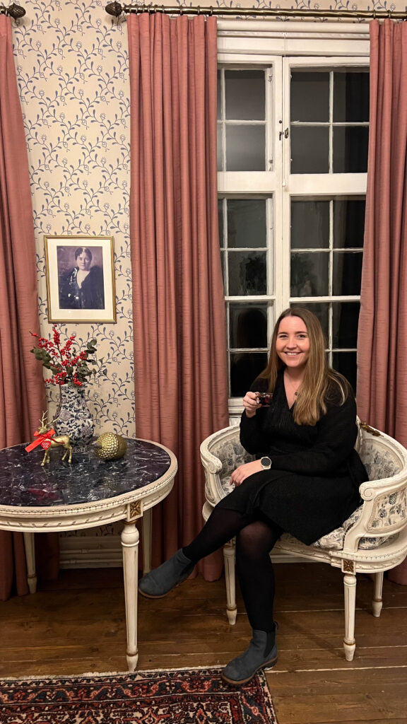 smiling woman in a christmas decorated room sitting in a chair holding a cup of mulled wine