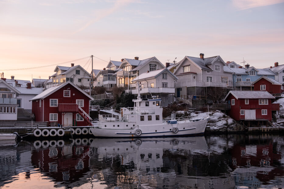 trehus og en fiskebåt på klädesholmen med refleksjoner i vannet i forgrunnen