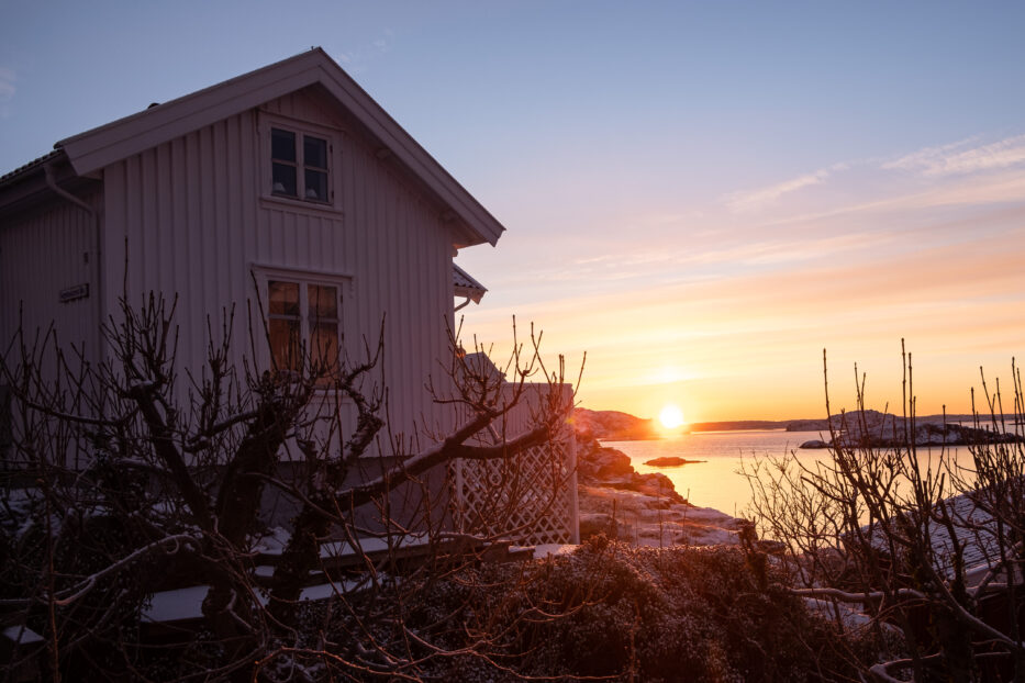 soloppgang over sjøen og et hvitt trehus i forgrunnen