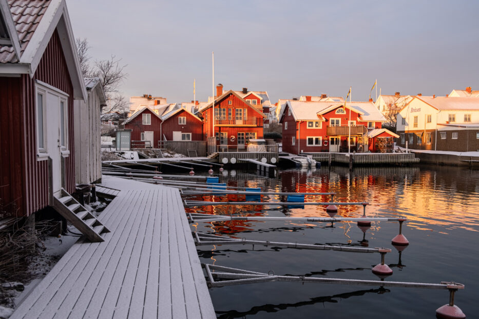 røde trehus dekket i snø og sol nær havet på klädesholmen